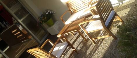 A wooden outdoor seating area with chairs and a table, surrounded by gravel and a potted plant.