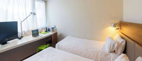 Habitación de hotel con dos camas, un escritorio, una computadora portátil, una lámpara y una ventana con cortinas.