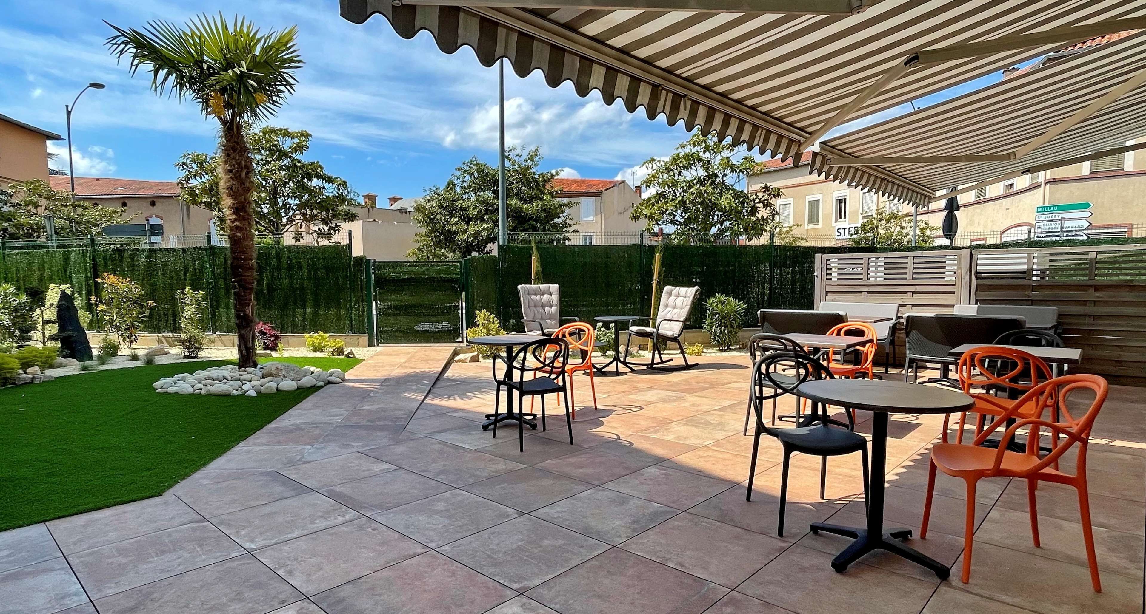 An outdoor patio area with tiled flooring, outdoor furniture, and a palm tree.
