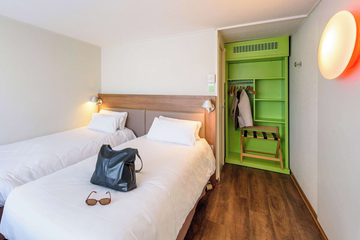 Habitación de hotel con dos camas, un armario verde y unas gafas de sol sobre la cama.