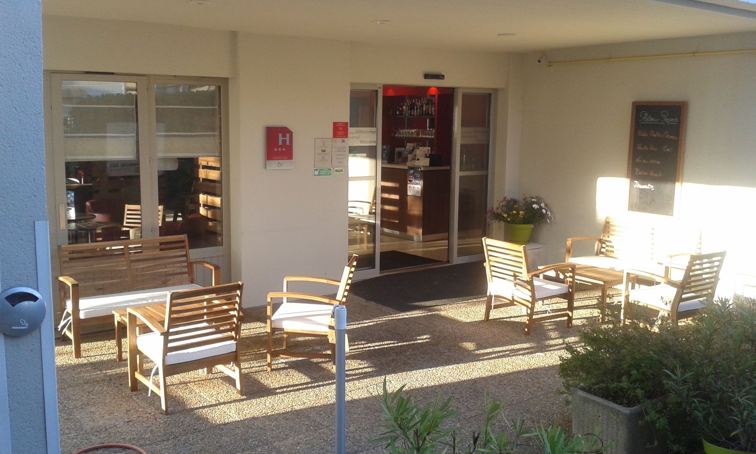 Un espacio al aire libre con mesas y sillas de madera, una pequeña entrada y un cartel.
