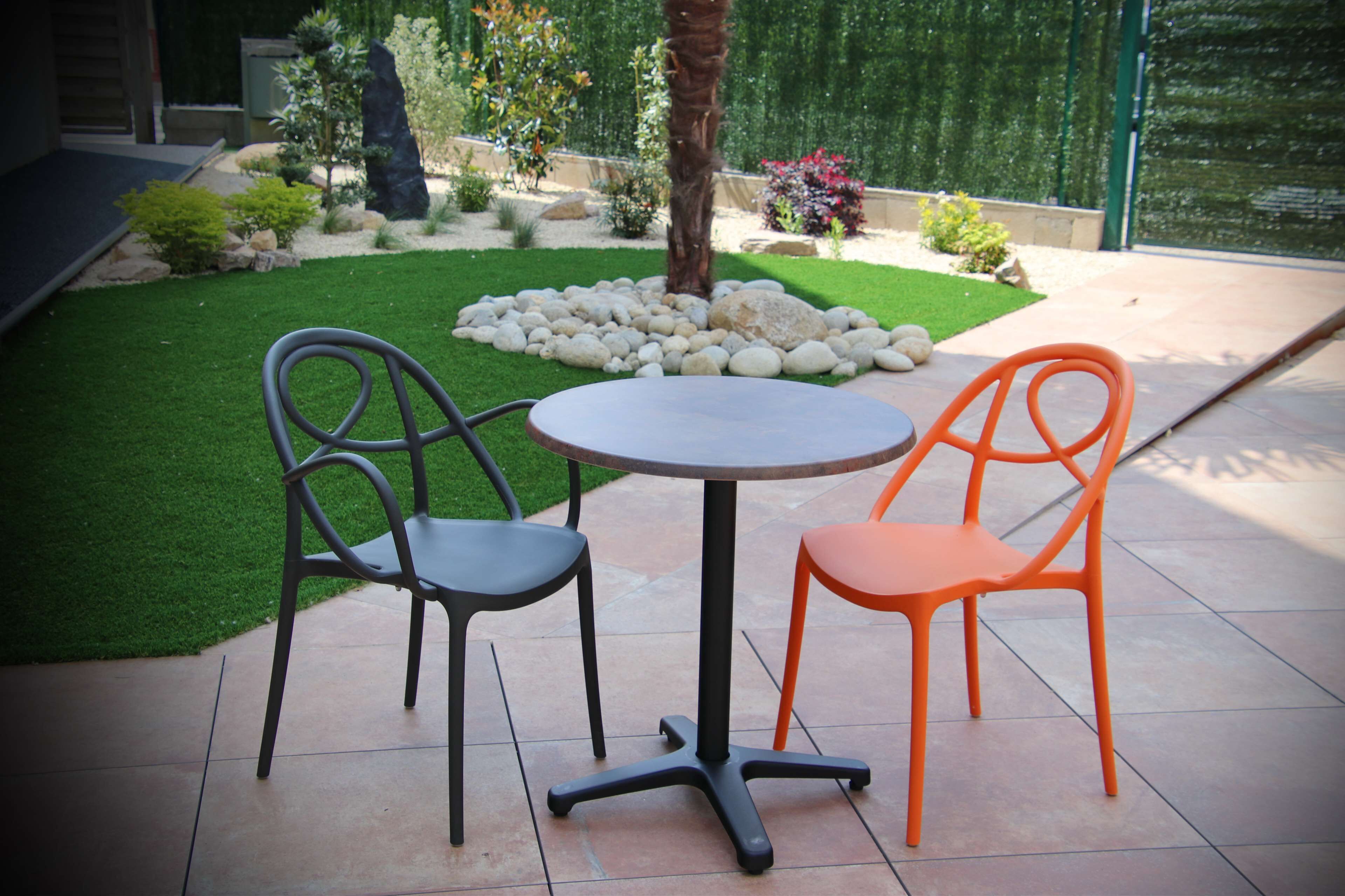 Un patio con dos sillas y una mesa, rodeado de un jardín cuidado con rocas y plantas.