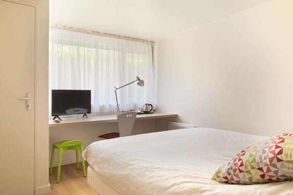 Un dormitorio con una cama, un escritorio con computadora, una silla, un ventanal con cortinas y un taburete verde.