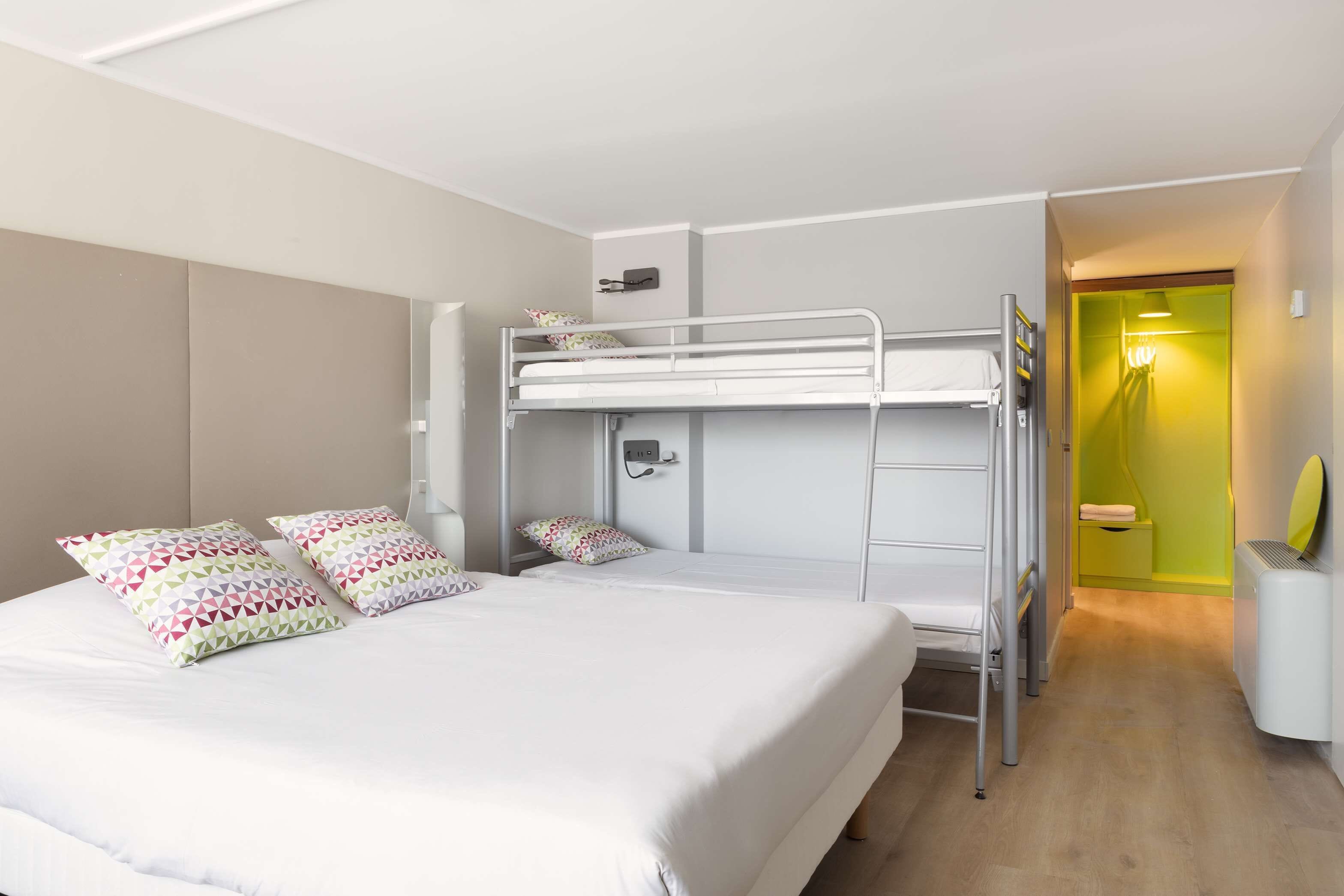 A bunk bed room with a white bed, two pillows, a bedside table, and a small nightstand.
