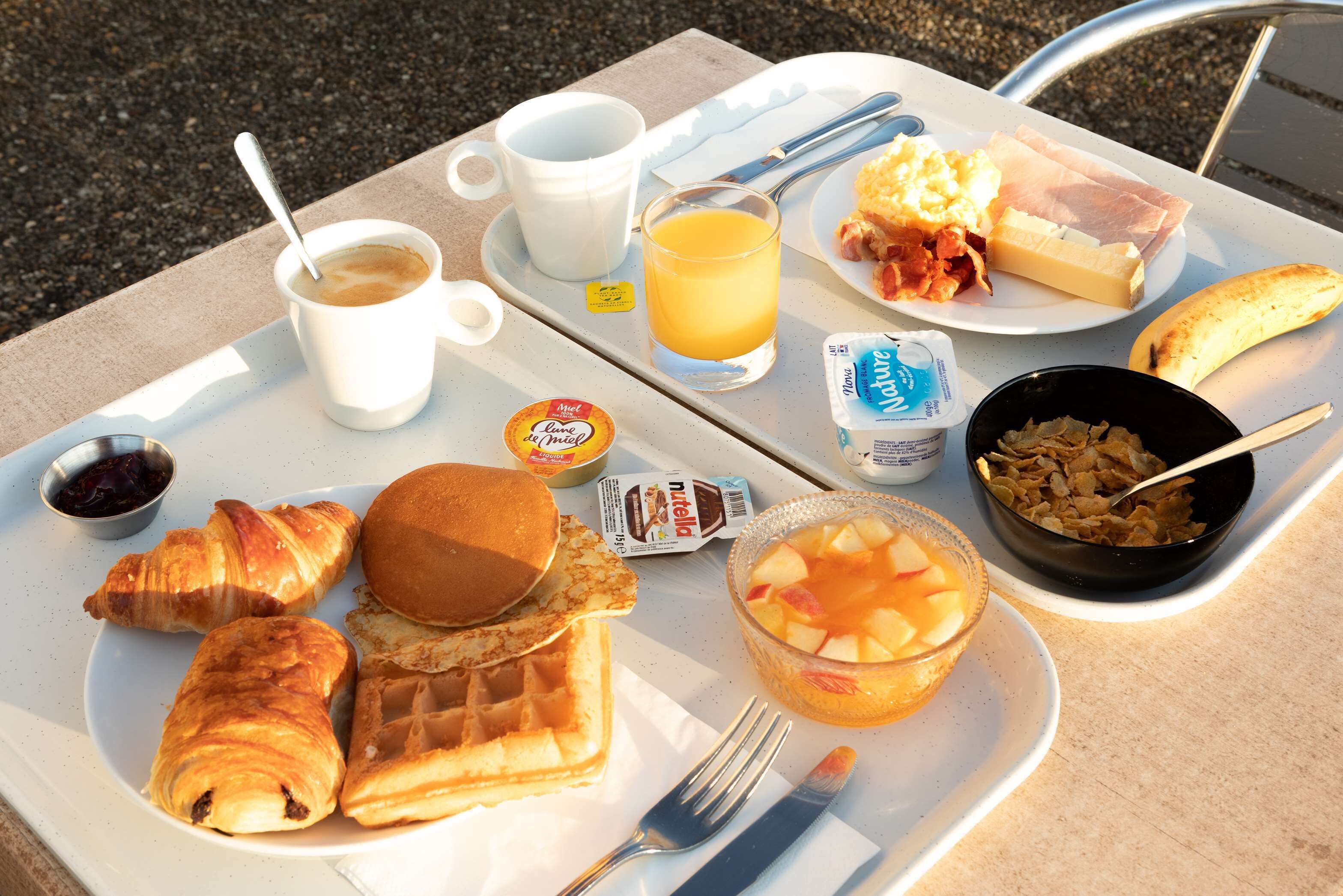 A breakfast tray with croissants, waffles, fruit, and beverages.