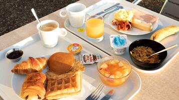 A breakfast tray with croissants, waffles, fruit, and beverages.