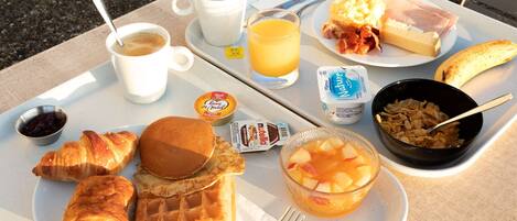 A breakfast tray with croissants, waffles, fruit, and beverages.