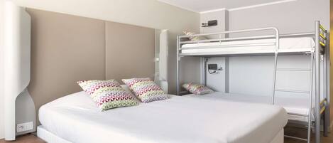 Quarto de hotel moderno com uma cama grande, uma cama beliche e uma mesa de cabeceira.