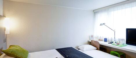 A hotel room with a bed, a desk, a chair, a TV, and a window with curtains.