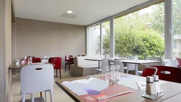 Un espace de restauration moderne, doté de tables et de chaises, de grandes fenêtres et offrant une vue sur la verdure environnante.