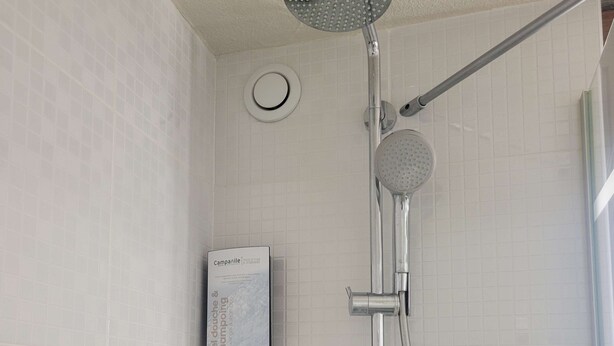 Doccia con soffione a mano e soffione circolare a parete, erogatore di sapone e un piccolo ripiano.