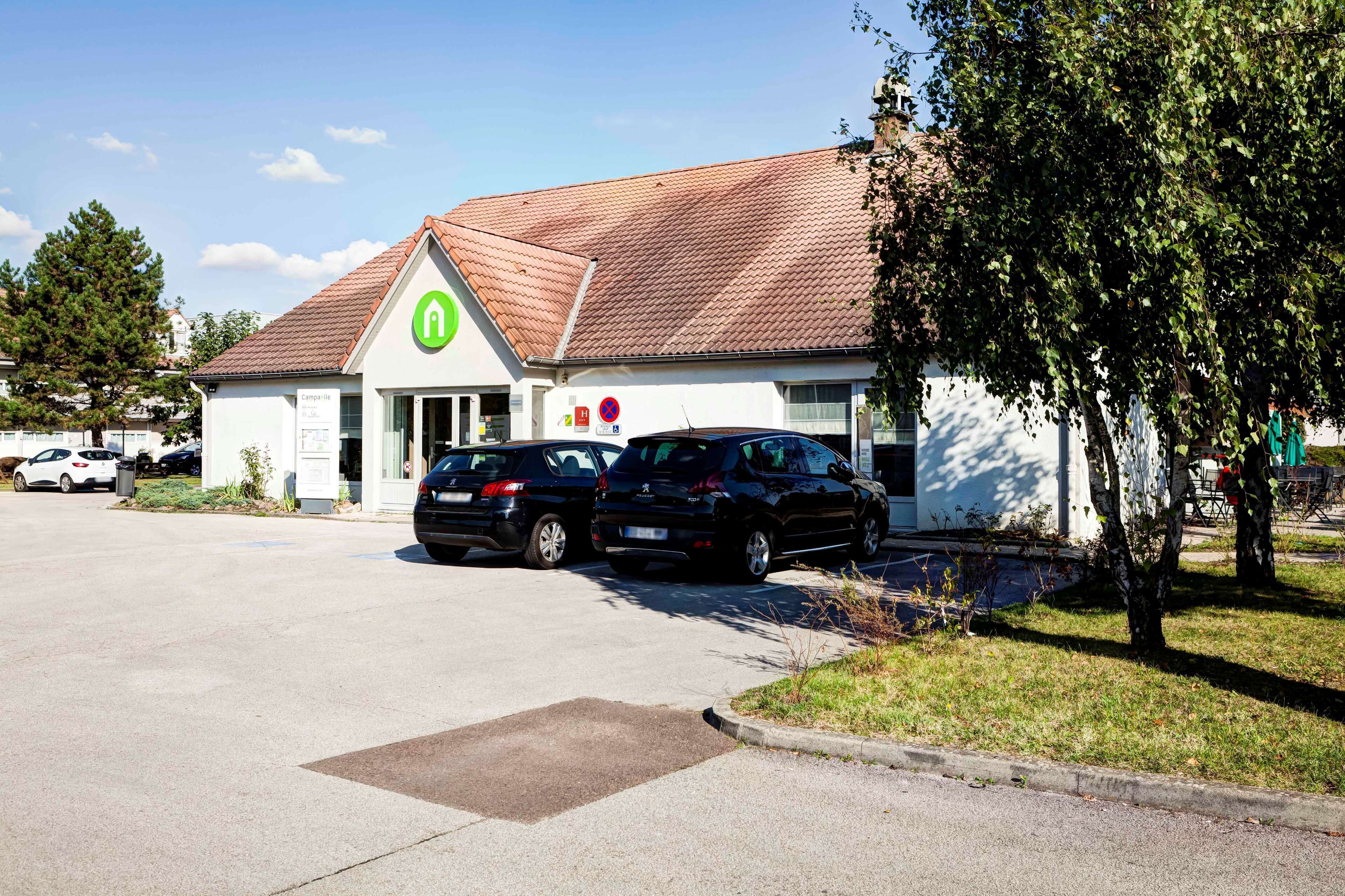 A building with a green logo, parked cars, and a clear sky.