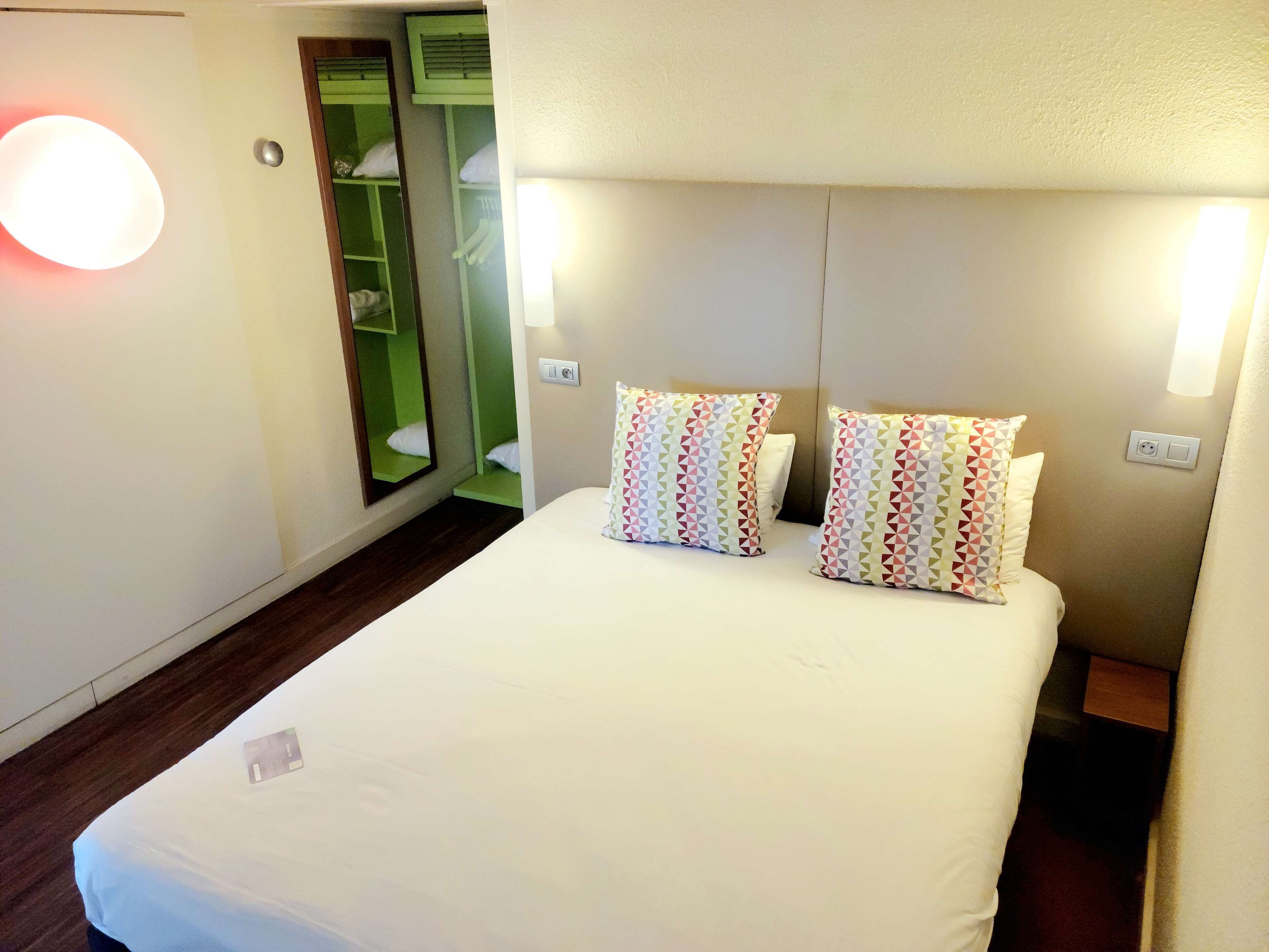 Habitació d'hotel amb un llit, dos almoinos, una tauleta de nit, un mirall i un armari.