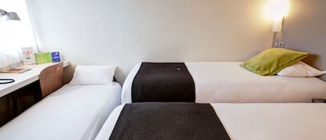 Habitación de hotel con dos camas individuales, un escritorio con lámpara y una mesita de noche con lámpara.
