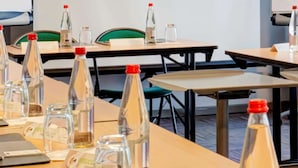 Une salle de conférence équipée de tables disposées pour les réunions, chacune agrémentée de plaques nominatives, de bouteilles d’eau et de verres.