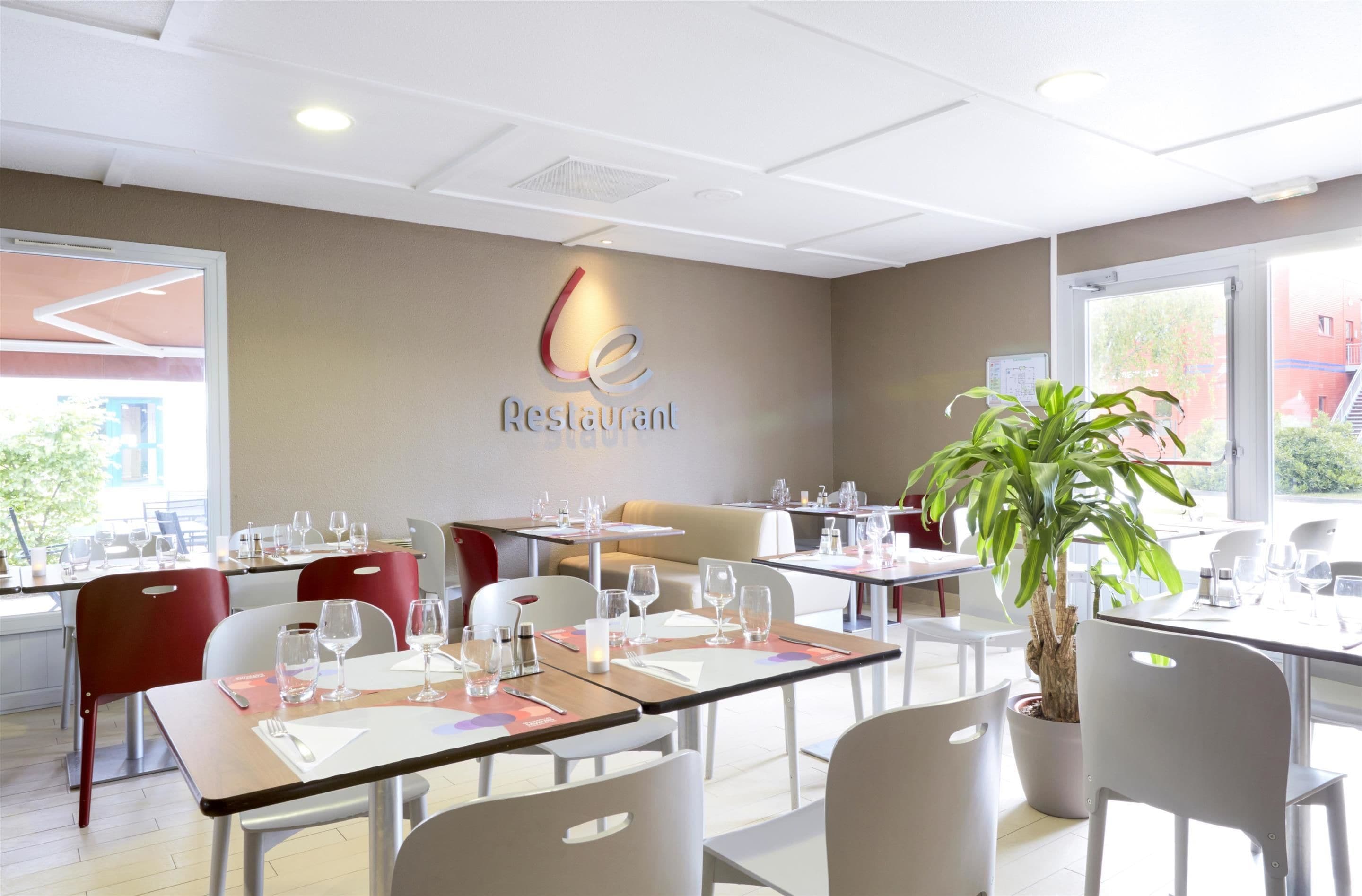 A restaurant interior with tables set for dining, a potted plant, and a sign on the wall.