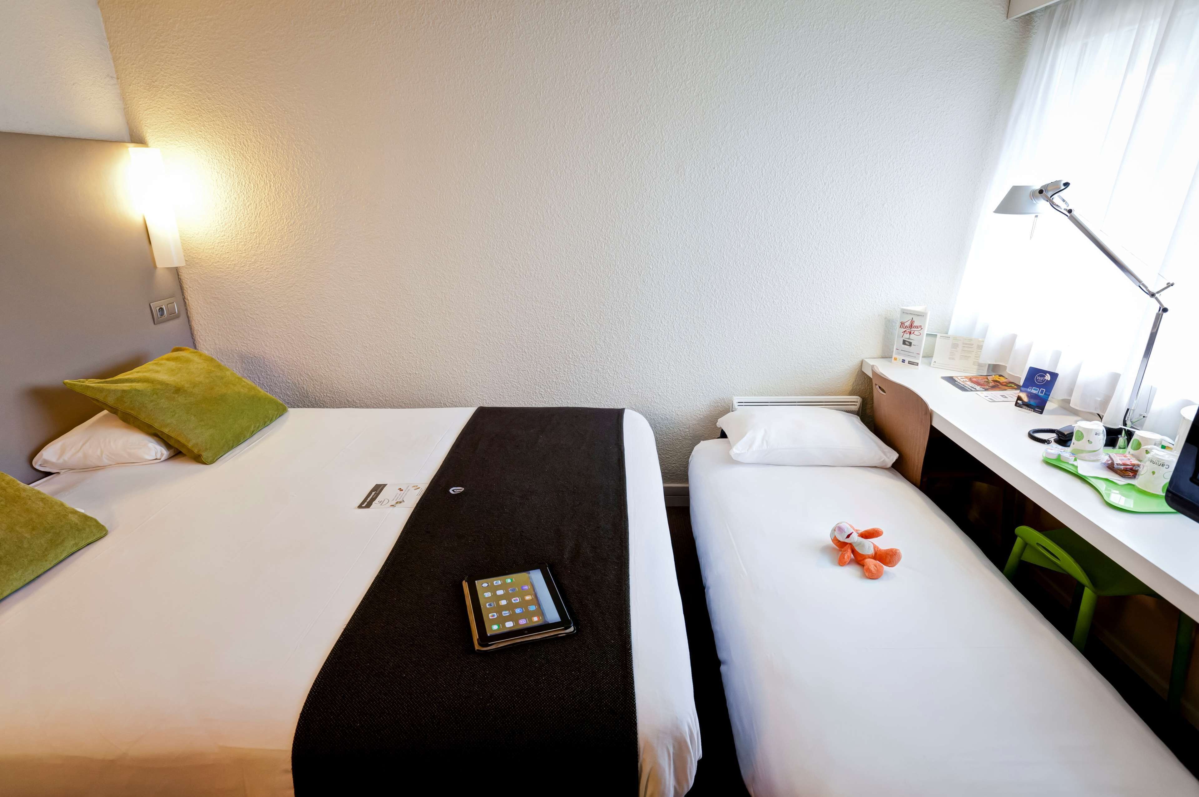 A hotel room with two beds, a desk with a lamp, a chair, and a window with curtains.