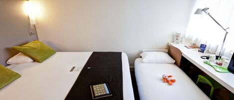A hotel room with two beds, a desk with a lamp, a chair, and a window with curtains.