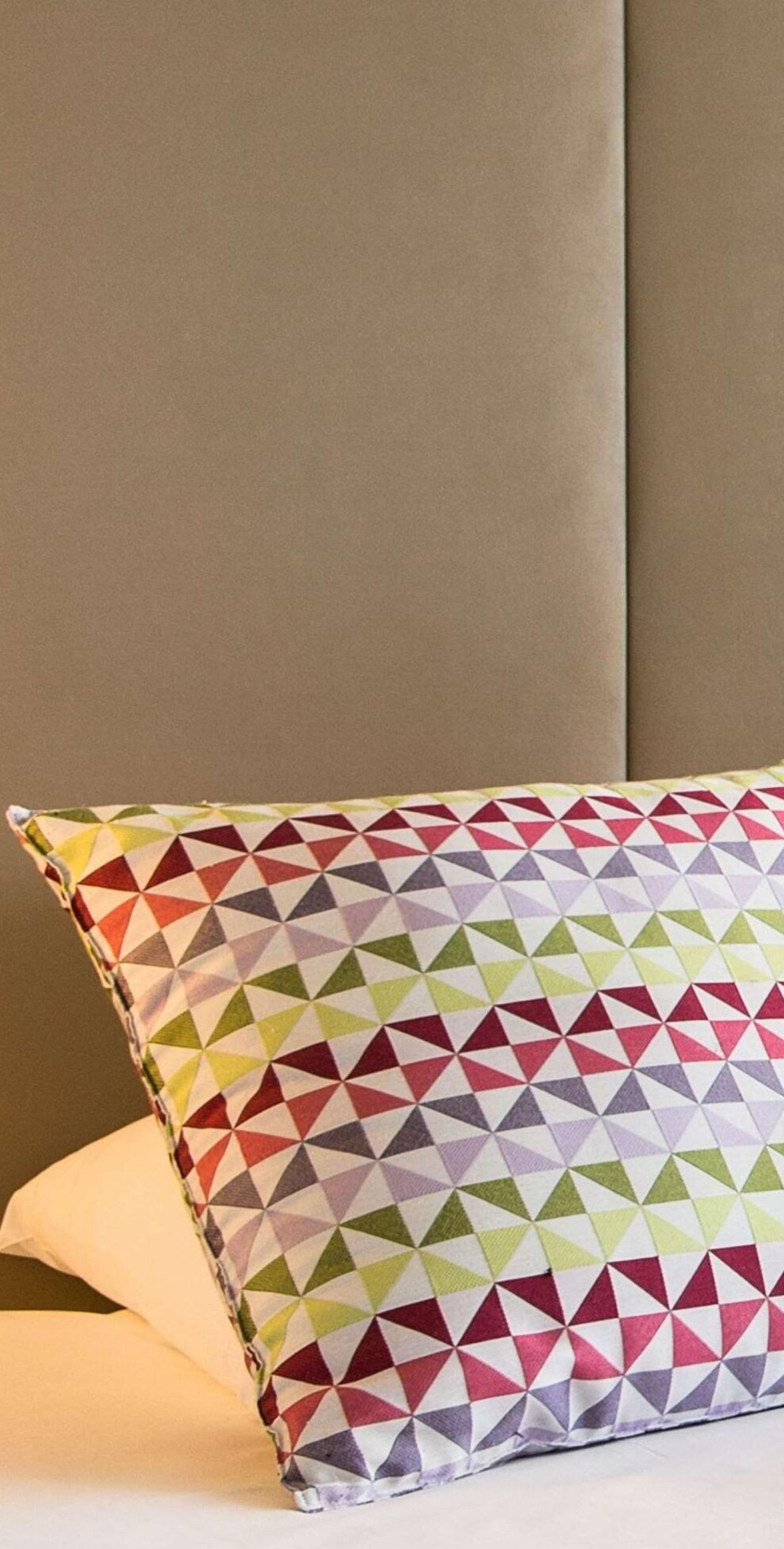 Een kussen met een kleurrijk geometrisch patroon op een bed.