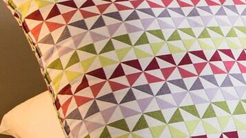 Een kussen met een kleurrijk geometrisch patroon op een bed.
