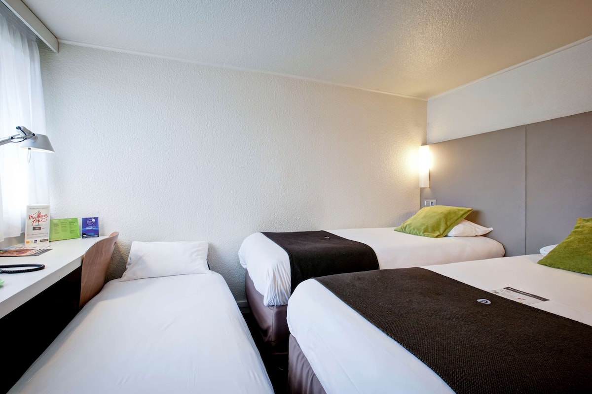 A hotel room with two single beds, a desk with a lamp, and a nightstand with a lamp.