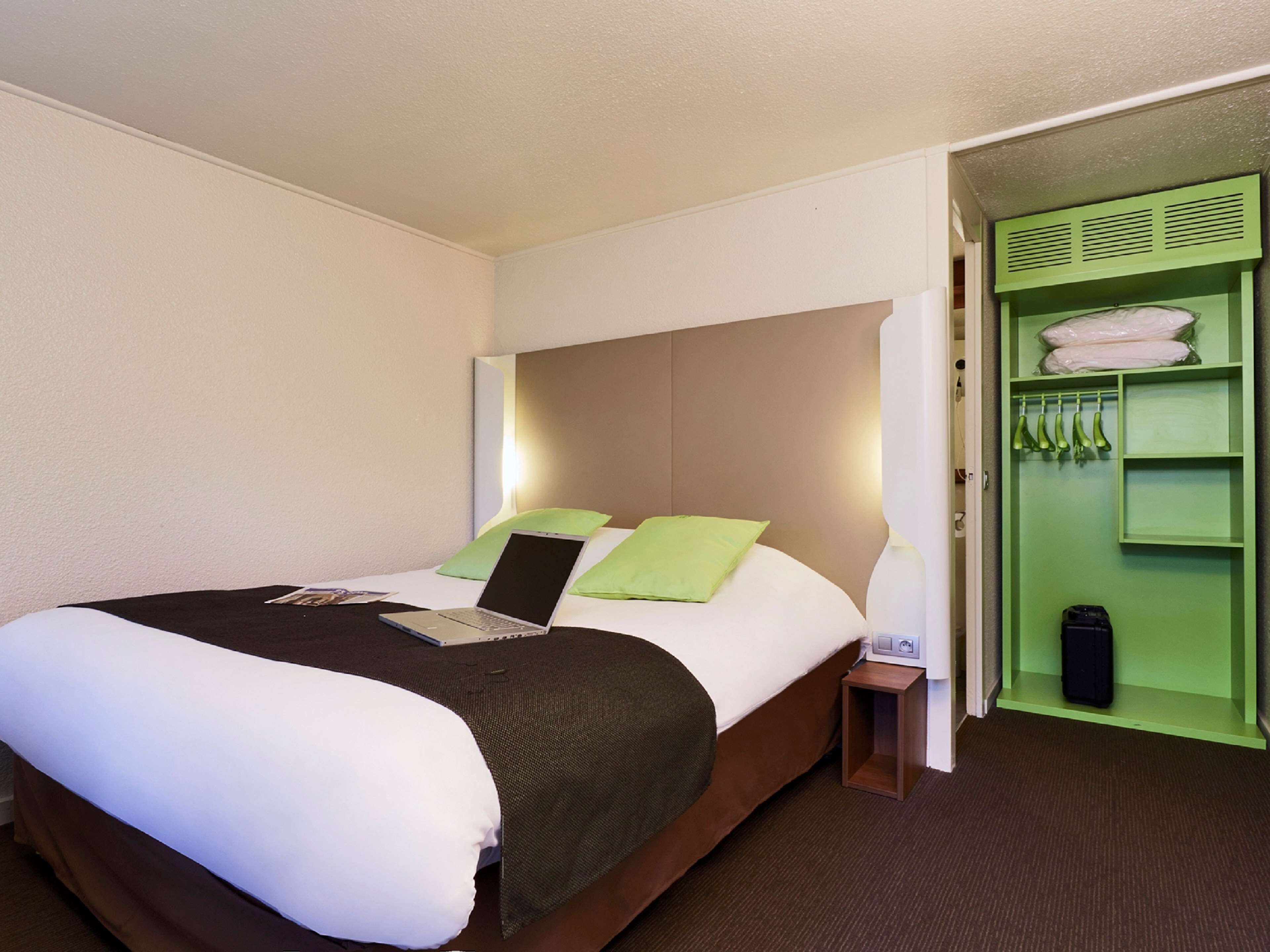 A hotel room with a bed, a laptop on the bed, a green closet, and a nightstand.