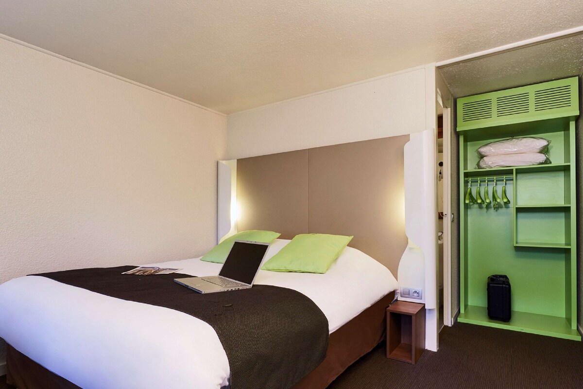 A hotel room with a bed, a laptop on the bed, a green closet, and a nightstand.
