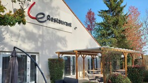 Un restaurante con terraza, una pérgola y un jardín cuidado.