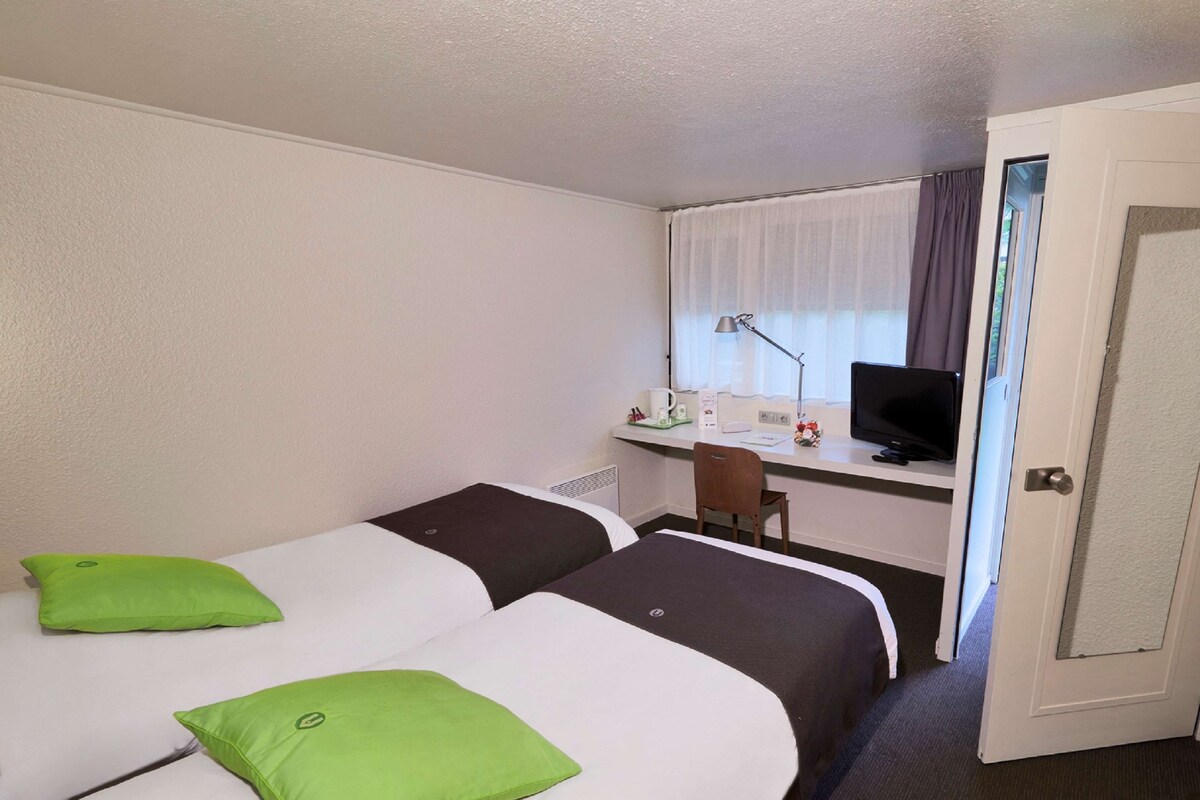 A hotel room with two beds, a desk with a computer and a TV, and a door.