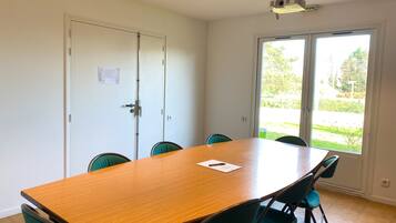 A conference room with a wooden table and green chairs, a white door, and a window with a view of greenery.