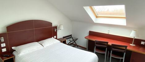 A bedroom with a bed, a desk, and a chair. There is a skylight above the desk.
