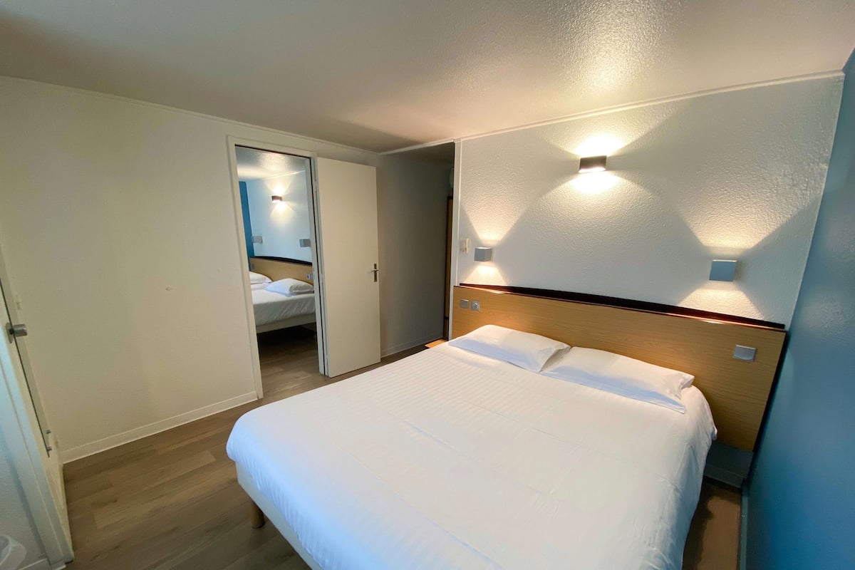 Una habitación de hotel con una cama grande, un cabecero de madera y dos lámparas fijadas a la pared.