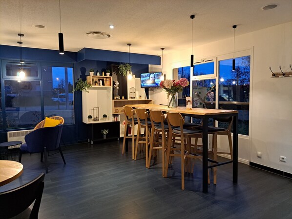 A modern dining area with a wooden table and chairs, a TV mounted on the wall, and a large window offering a view of the outside.