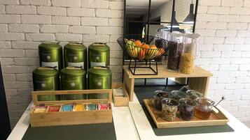 A buffet setup with green canisters, a fruit bowl, and various food items on trays.