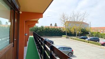 A balcony with a green mat, wooden railing, and a view of a parking lot with cars and buildings.