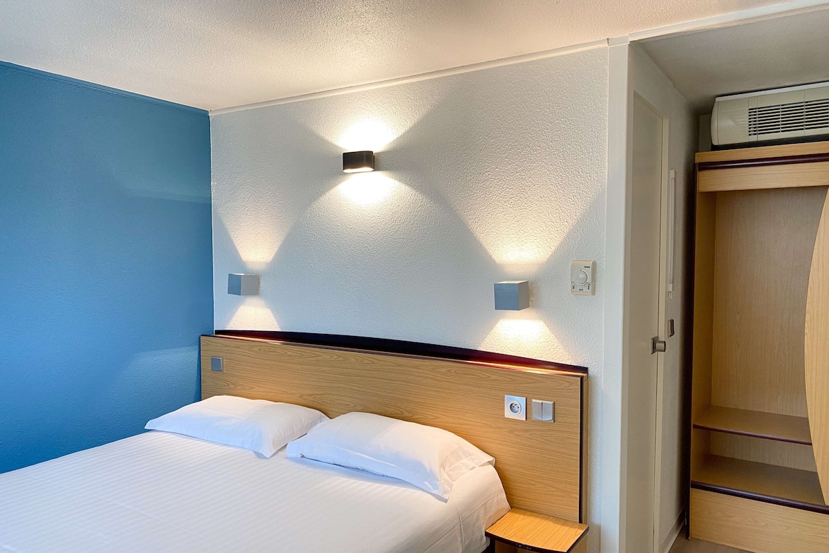 Una habitación de hotel con cama, mesitas de noche, armario e iluminación en la pared.