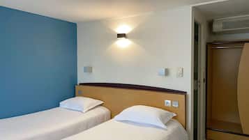 A hotel room with two single beds, a wall-mounted light, an air conditioning unit, and a wooden wardrobe.