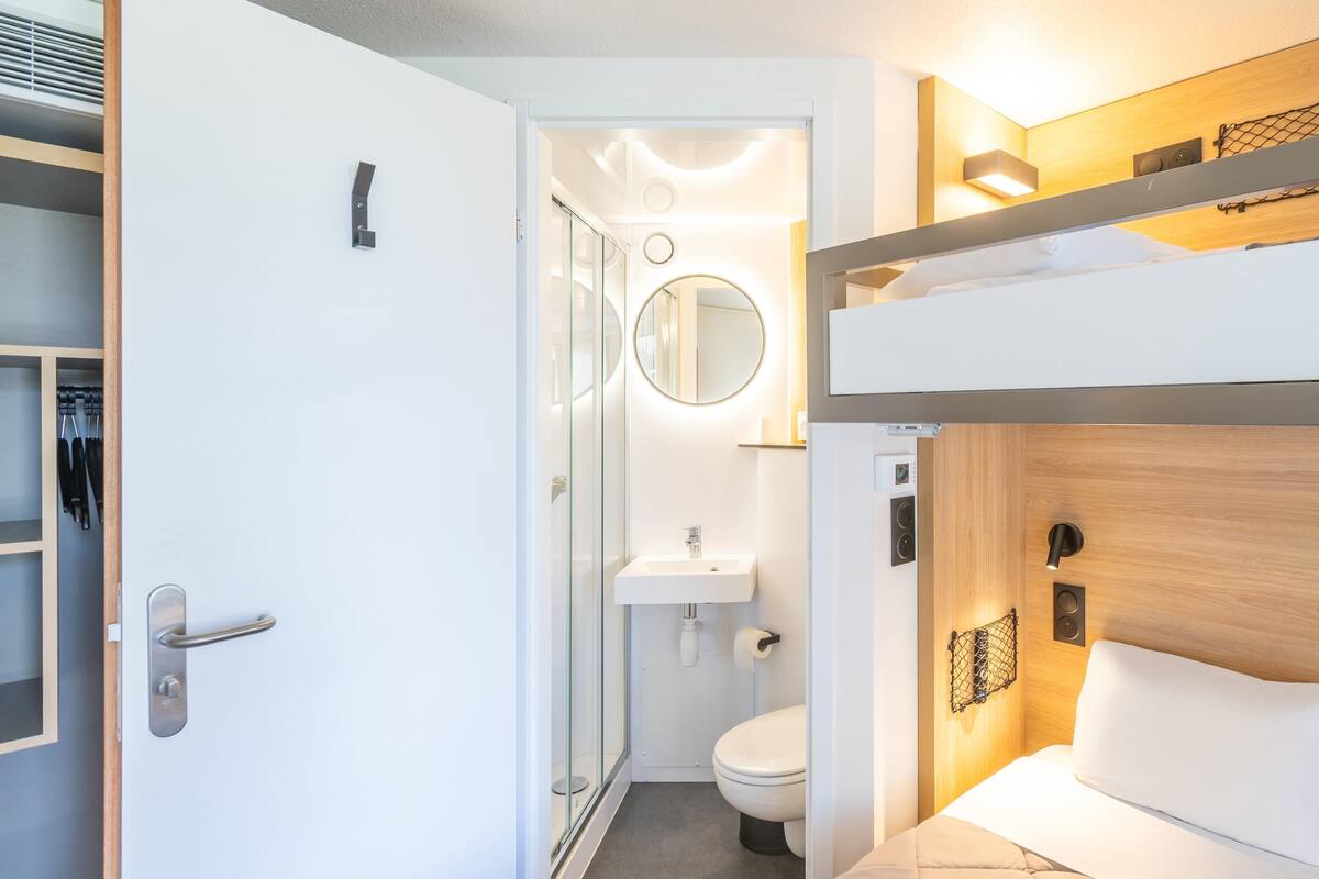 Een kleine hotelkamer met een stapelbed, een aparte badkamer en een kleine kast.