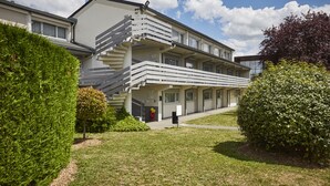 Un bâtiment moderne doté d’un escalier menant à un balcon, le tout entouré d’une végétation bien entretenue.