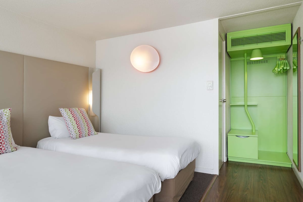 Une chambre d’hôtel avec deux lits, un applique murale ronde et une porte de salle de bain verte.