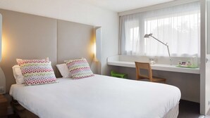 Une chambre d’hôtel avec un lit, un bureau, une chaise et une fenêtre avec des rideaux.