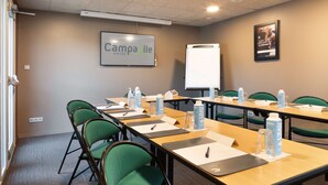 Une salle de conférence avec une longue table, des chaises vertes, des bouteilles d’eau, des plaques nominatives et un tableau blanc.