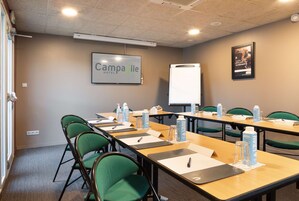 Un salón de conferencias con una larga mesa, sillas verdes, botellas de agua, tarjetas de identificación y una pizarra.
