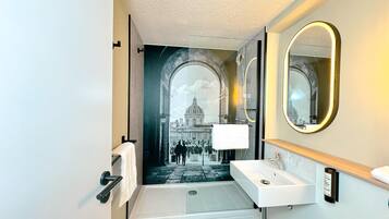A modern bathroom with a large mirror, a sink, and a shower.