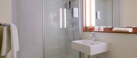 Un baño con ducha de vidrio, lavabo blanco y espejo sobre el lavabo.