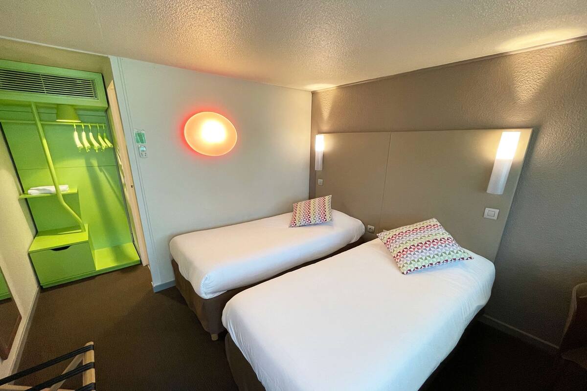 Ein Hotelzimmer mit zwei Einzelbetten, einer grünen Wandverkleidung und einer roten Wandleuchte.