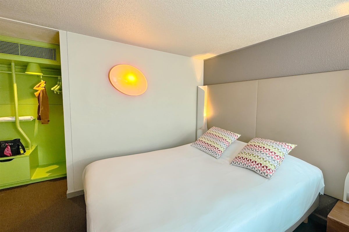 Ein Hotelzimmer mit einem Bett, einem grünen Kleiderschrank und einer Wandleuchte.