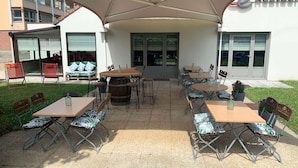 An outdoor patio area with multiple tables and chairs, a covered seating area, and a building entrance. - Campanile Epinay Sur Orge Savigny Sur Orge (Epinay-sur-Orge)