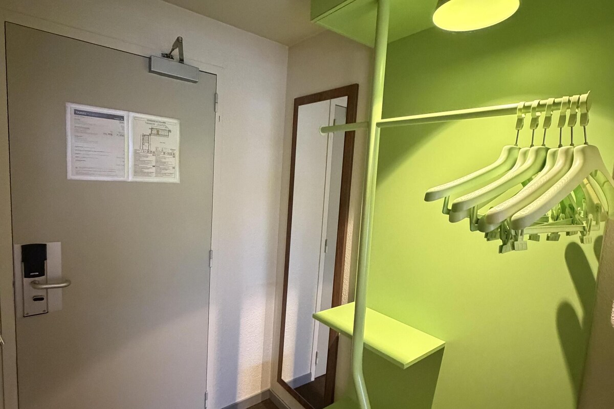A hallway with a green wall, a door with a sign, a coat rack, and a light fixture.