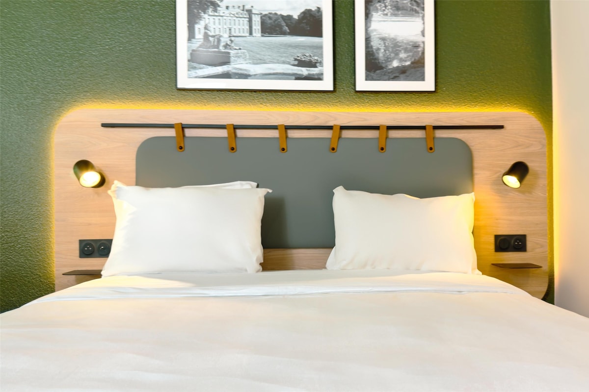 A neatly made bed with two pillows and a headboard with wall-mounted lights.